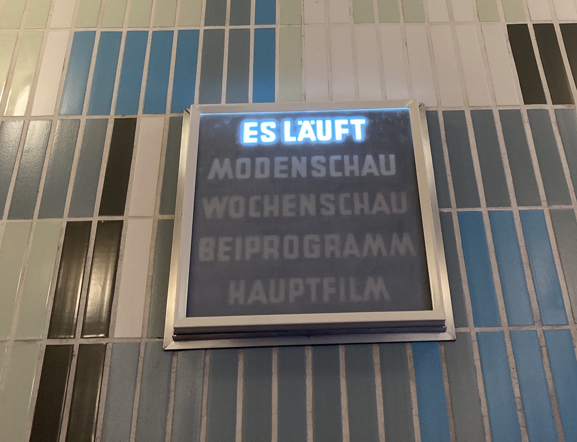 Leuchtschild mit fünf Zeilen: Es läuft, Modenschau, Wochenschau, Beiprogramm, Hauptfilm an gefliester Wand