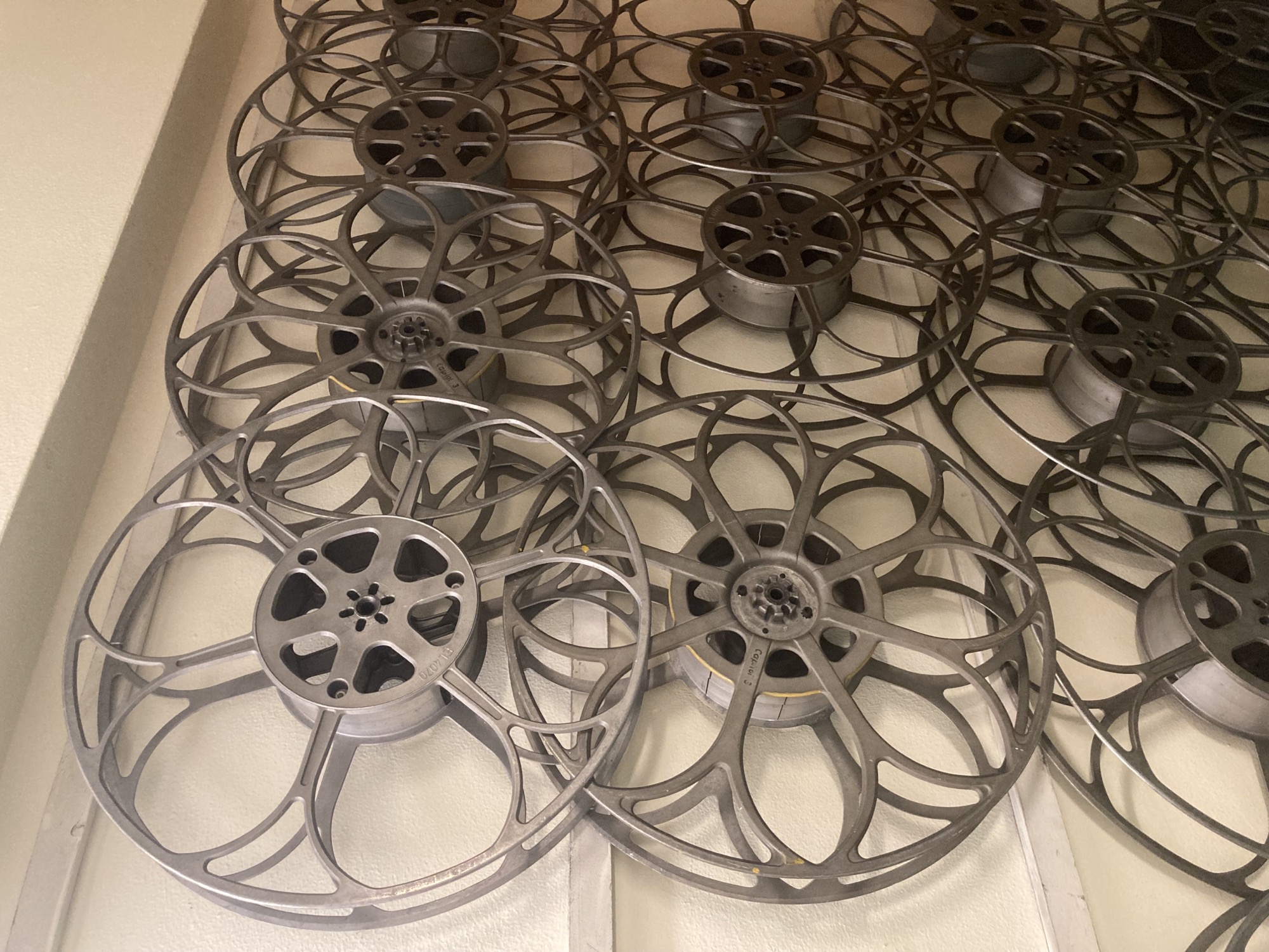 an einer Wand sind mehrere nicht benutzte Filmspulen aufgehängt, die Speichen der Spulen haben die Form von Blütenblättern